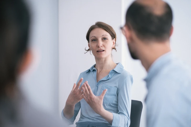 Frau spricht in einer Therapiesitzung mit zwei anderen Personen.